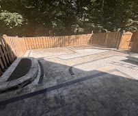 Outdoor backyard patio with stone paving, curved steps, and a wooden fence in sunlight