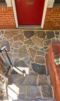 Stone entry walkway and steps leading up to a red front door, with a black handrail.