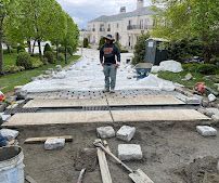 Worker laying paving stones on a garden walkway in front of a building