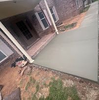 Tilted view of a house porch with columns, brick steps, and a freshly poured concrete driveway