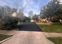 Quiet suburban street with fresh black asphalt, trees, grass lawns, and houses under a partly cloudy sky