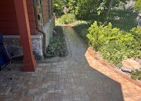Brick patio walkway beside a house, curving through green shrubs and a garden path.
