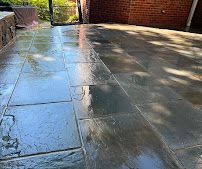 Wet stone patio with sunlight reflections beside a brick wall and gate