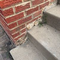 Concrete steps beside a brick wall with chipped mortar at the base