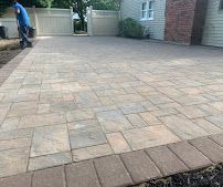 Stone-paved driveway or courtyard with a person working near a gate in the background