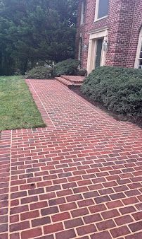 Brick walkway beside a brick house, bordered by shrubs and lawn