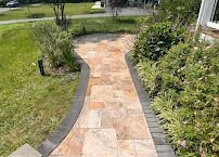 Curved stone walkway bordered by grass and shrubs leading to a house entrance