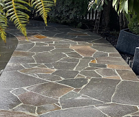 Stone garden walkway bordered by plants and a black planter