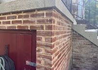 Brick building corner with red door and metal staircase beside a sloped roof.
