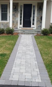 Stone walkway leads to a front door of a suburban house with brick edging and green lawn.