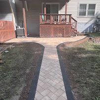 Brick walkway leading to a small wooden porch with red railing in a front yard