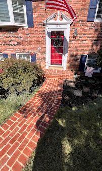 Brick front walkway leading to a red front door with an American flag above it.