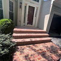 Brick front steps leading to a brown front door beside a garage, with shrubs and sunlight on the walkway