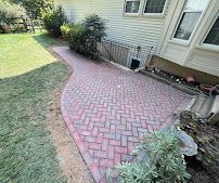 Brick-paver walkway curving beside a house and lawn with shrubs along the edge