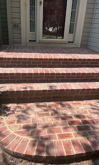 Brick front steps leading to a house entrance with a white doorframe and shadowed porch.