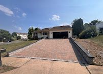 Suburban house with a wide brick driveway, garage, and landscaped front yard under a blue sky