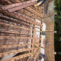 Wooden deck frame under construction with exposed beams, fencing, and building materials outdoors.