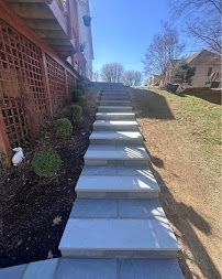 Concrete outdoor stairs beside a house, with a wooden lattice wall and sloped lawn on a sunny day
