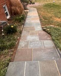 Stone walkway beside a house, bordered by grass and plants, with a slight curve
