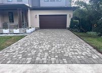Home with a wide stone-paver driveway leading to a two-car garage and porch.