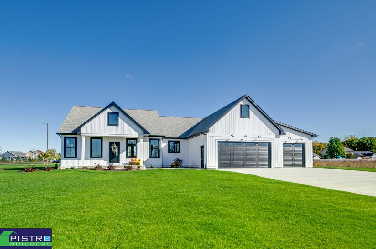 A white house with a black roof is sitting on top of a lush green field.