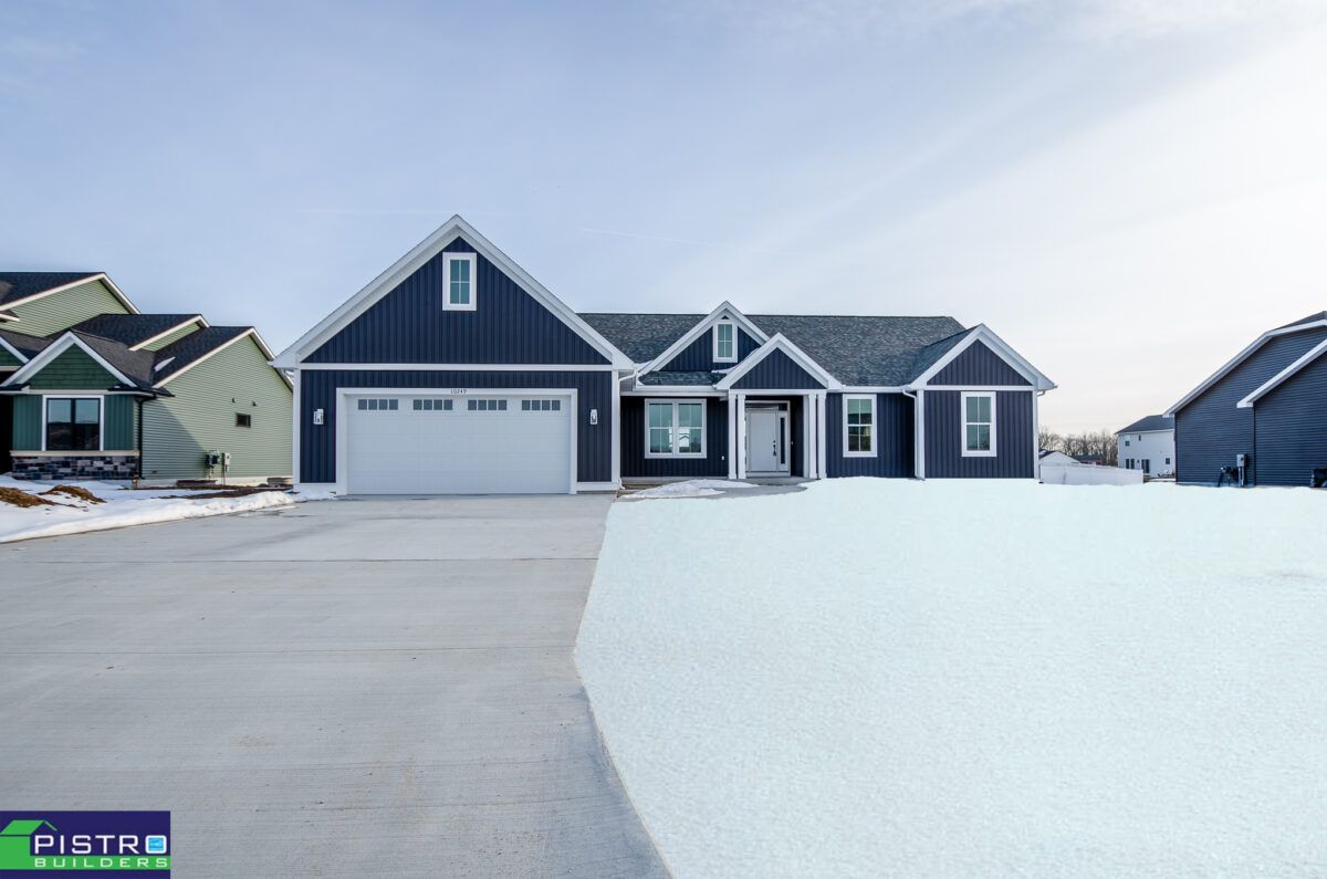 A blue house with a white garage door is surrounded by snow.