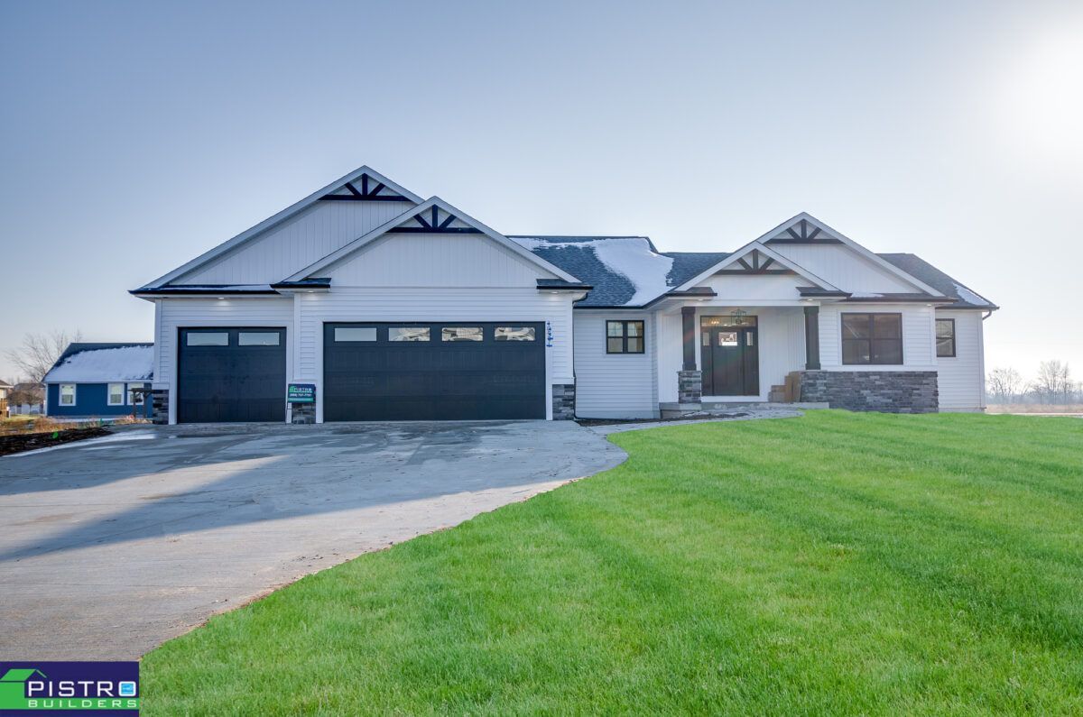 A large white house with a black garage door is sitting on top of a lush green field.