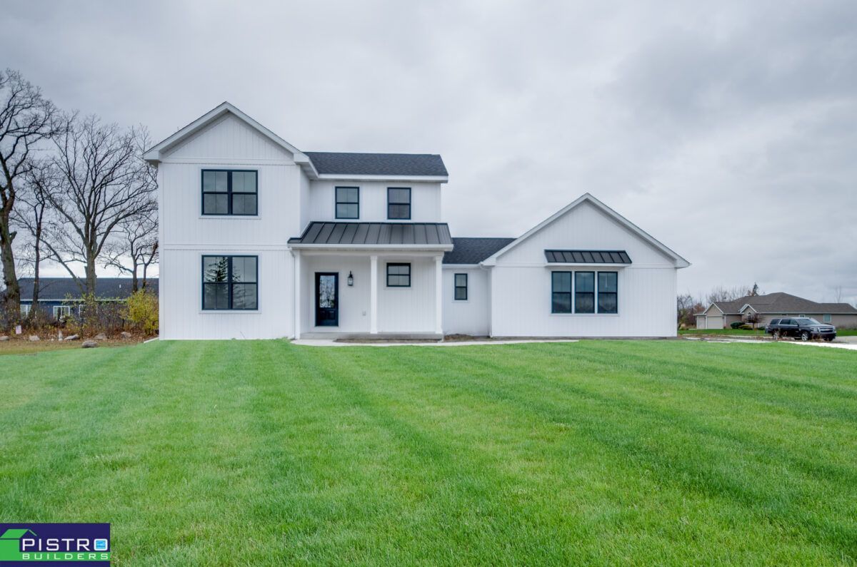 A white house with a black roof is sitting on top of a lush green field.