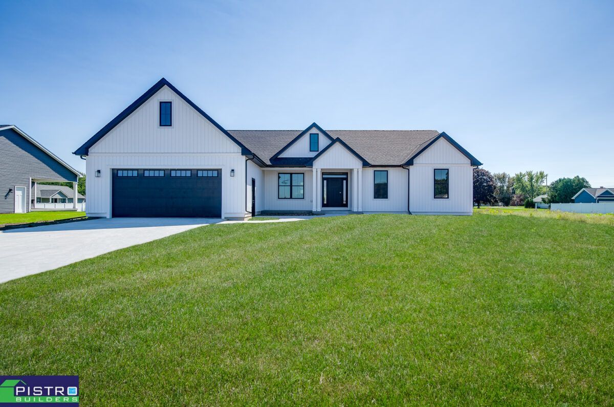 A white house with a black garage door is sitting on top of a lush green field.