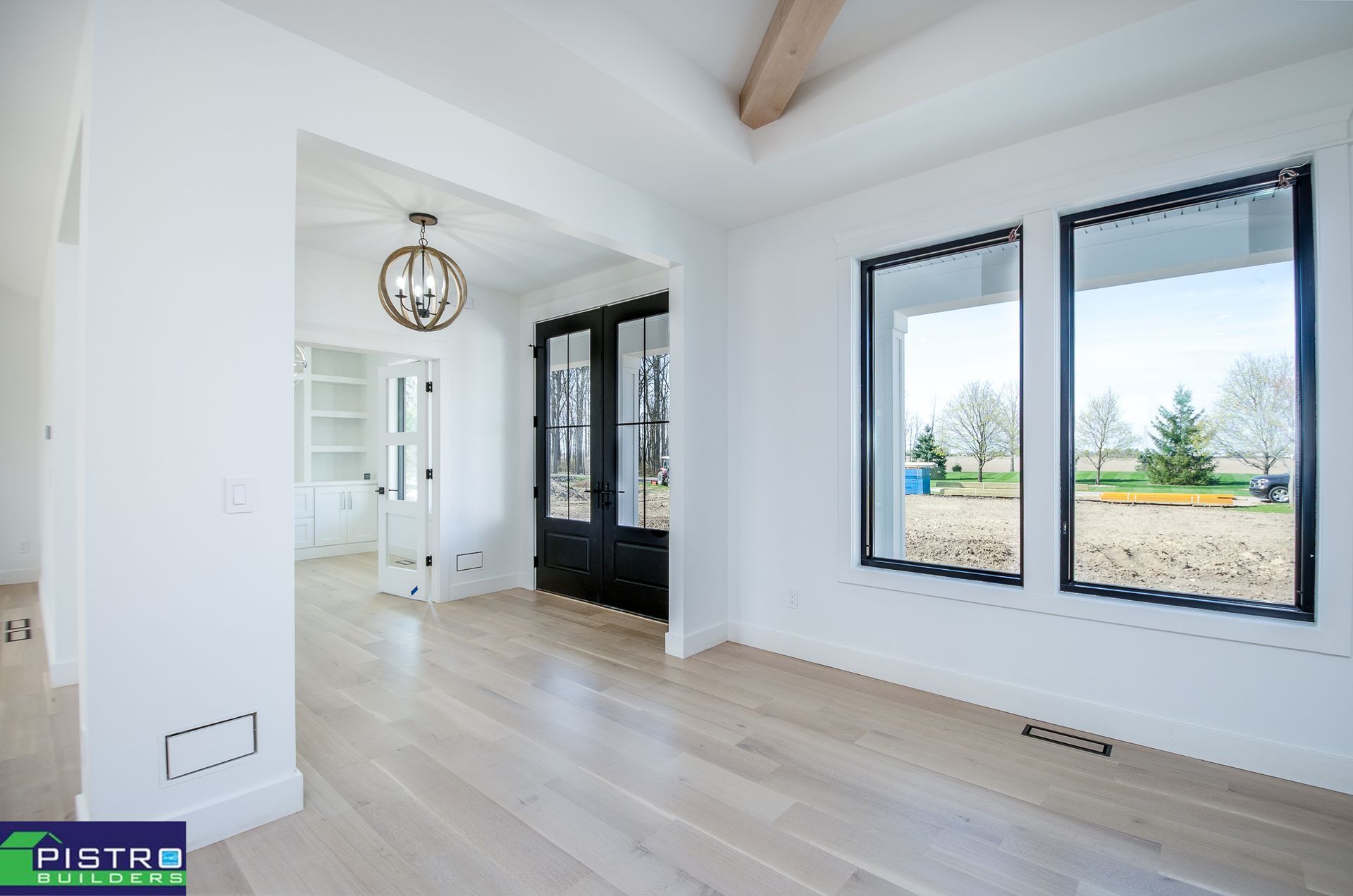 Bright white interior with light wood floors, black framed windows, and a doorway with black doors