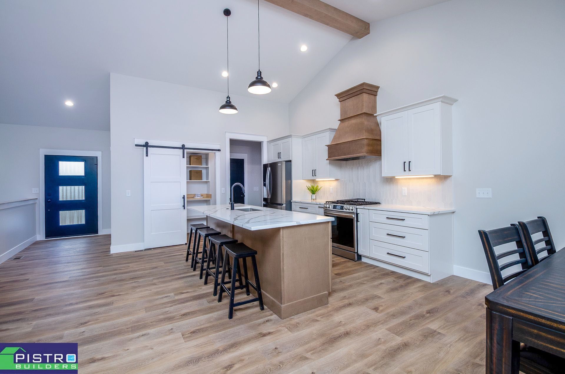 Modern kitchen with white cabinets, island with stools, and wooden range hood