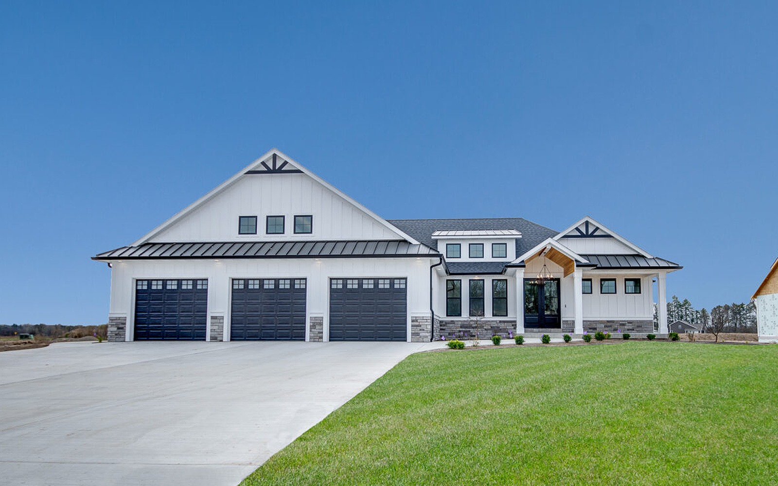 A large white house with black garage doors is sitting on top of a lush green lawn.