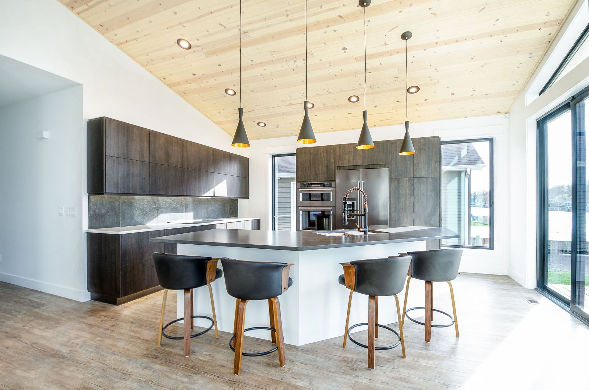 Modern kitchen with island, dark cabinets, wood ceiling, pendant lights, and bar stools