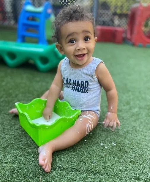 Smiling child sitting on artificial grass, playing with a green sand tray and white sand