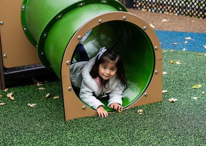 Child crawling through a green playground tunnel, reaching out on artificial turf