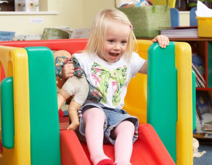 Smiling child on a colorful indoor slide, holding the green side panel.