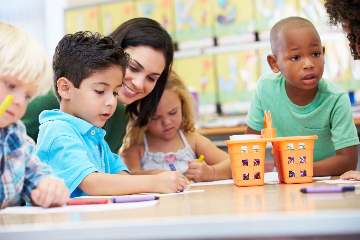 Children and a teacher working together at a classroom table with books and orange blocks