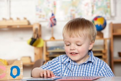 Young child in a blue plaid shirt smiling and playing with a book at a classroom table