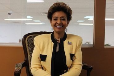 Smiling woman in a cream blazer seated in an office chair, with a bright office background