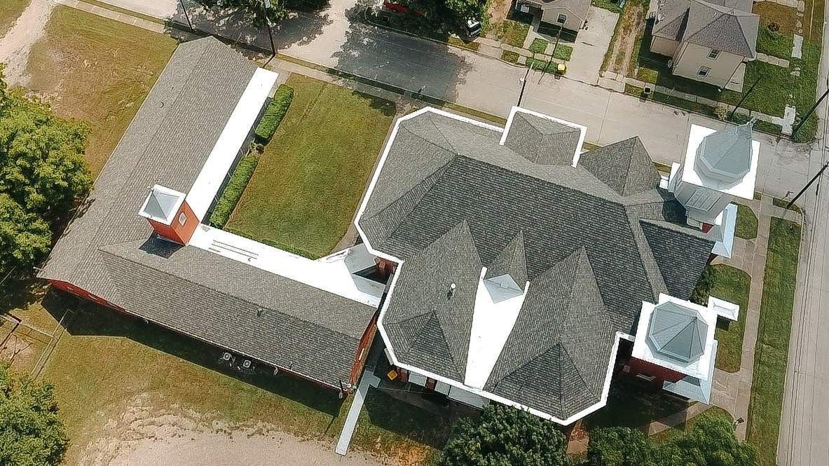 Aerial view of a red-roofed, multi-section building with two turrets and an attached L-shaped structure.