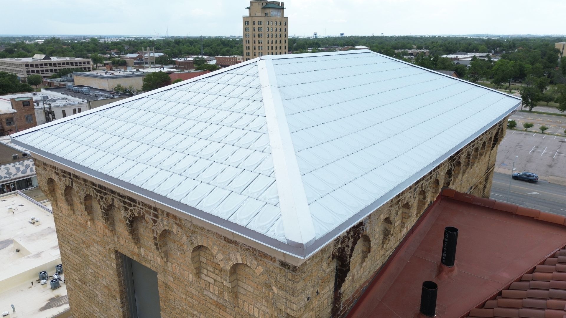 Aerial view of building with metal roof; red tile roof on lower section.
