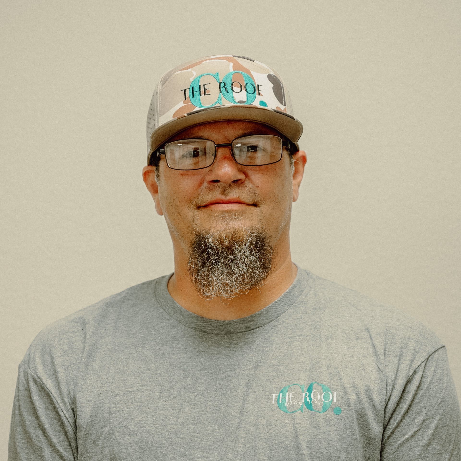 Man with glasses and goatee wearing a hat and shirt with 