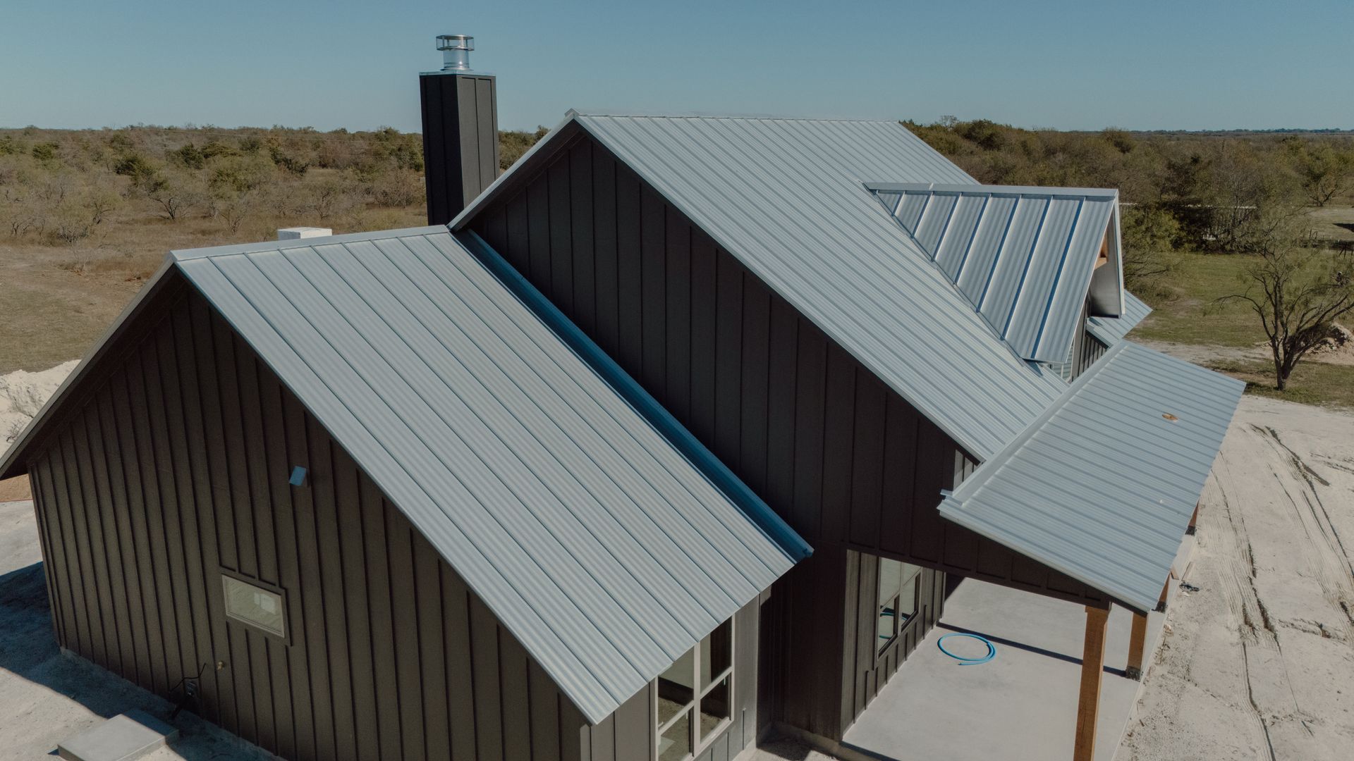 Dark gray house with silver metal roof under a clear blue sky.