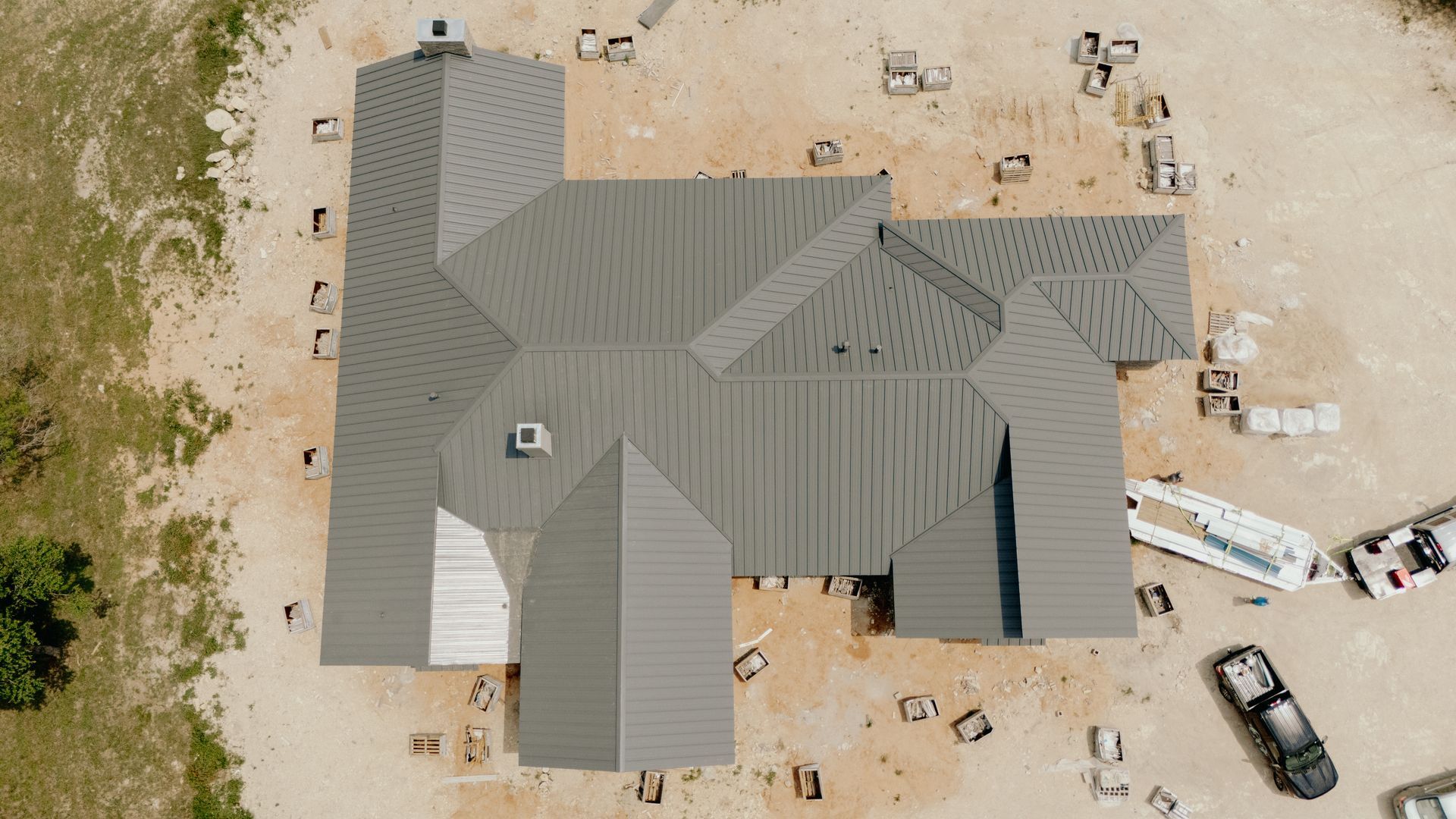 Aerial view of a gray-roofed house under construction on a dirt lot.