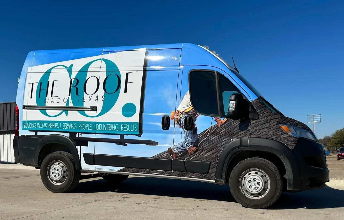 A van with "The Roof Go" logo and roofing scene graphics, against a blue sky. It's parked outside.