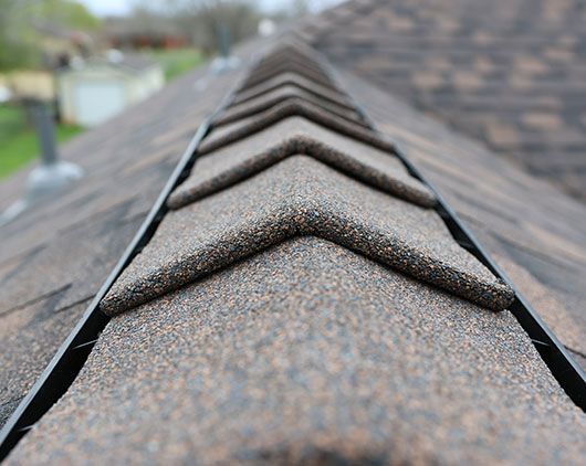 Close-up of a brown shingle roof ridge with overlapping shingles and dark metal edging