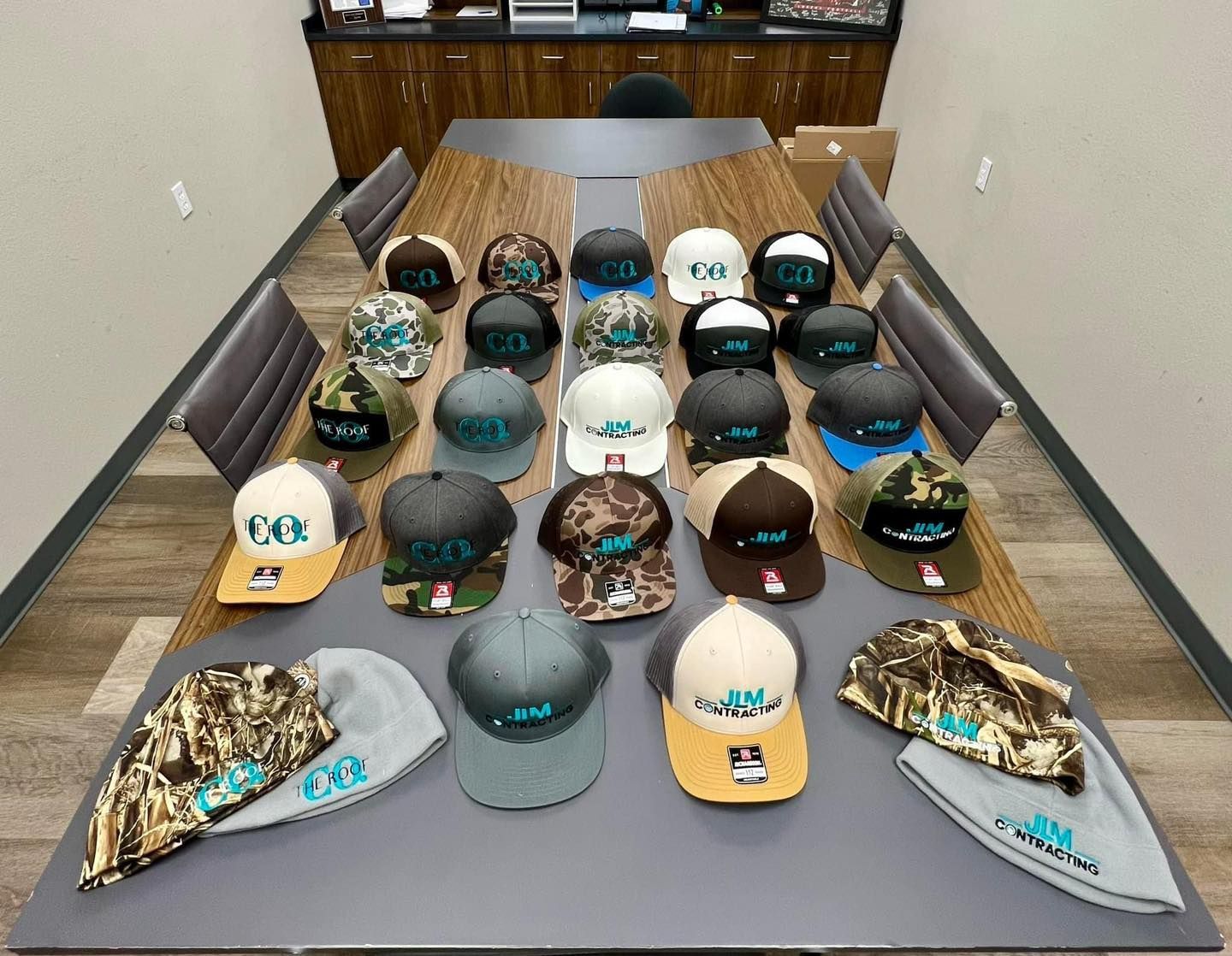A conference table displays a collection of baseball caps and knit hats with a turquoise logo.