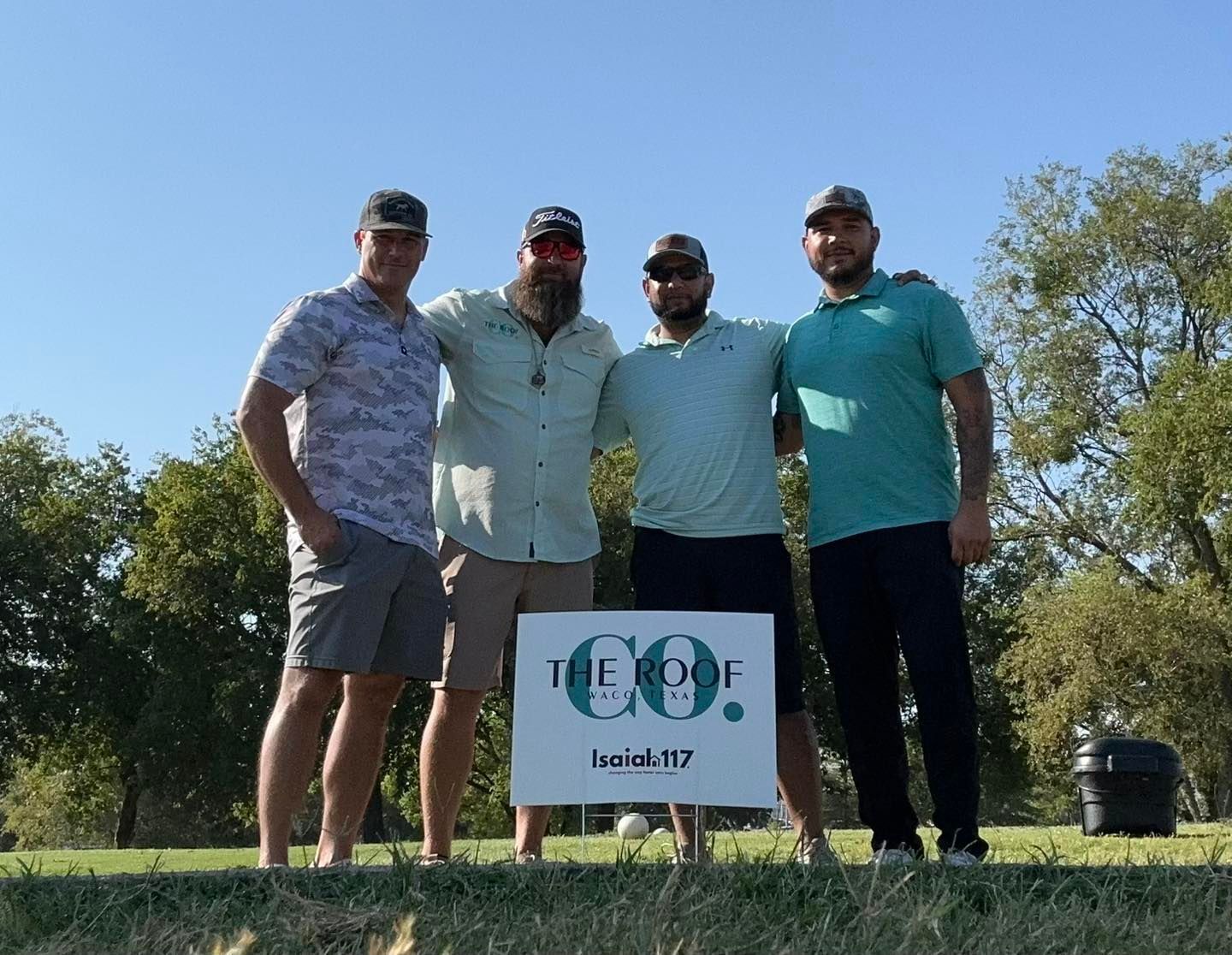 Four men standing on a golf course, posing with a sign for 