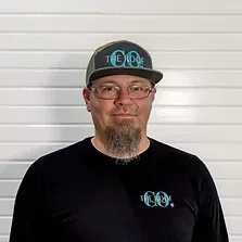 Man with glasses and goatee wearing a hat and shirt with 
