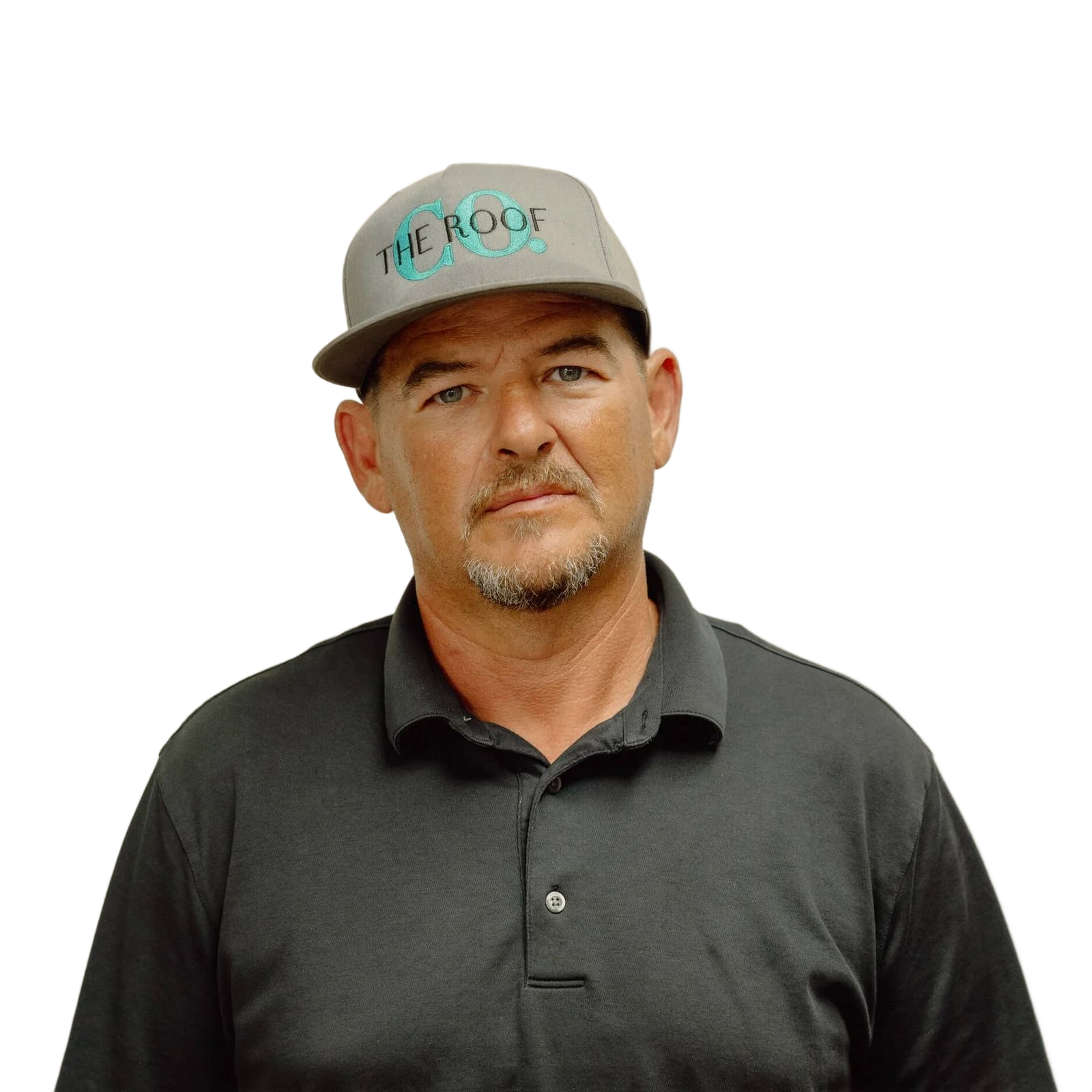 A man wearing a gray cap and shirt stands in front of a white wall. The cap reads 